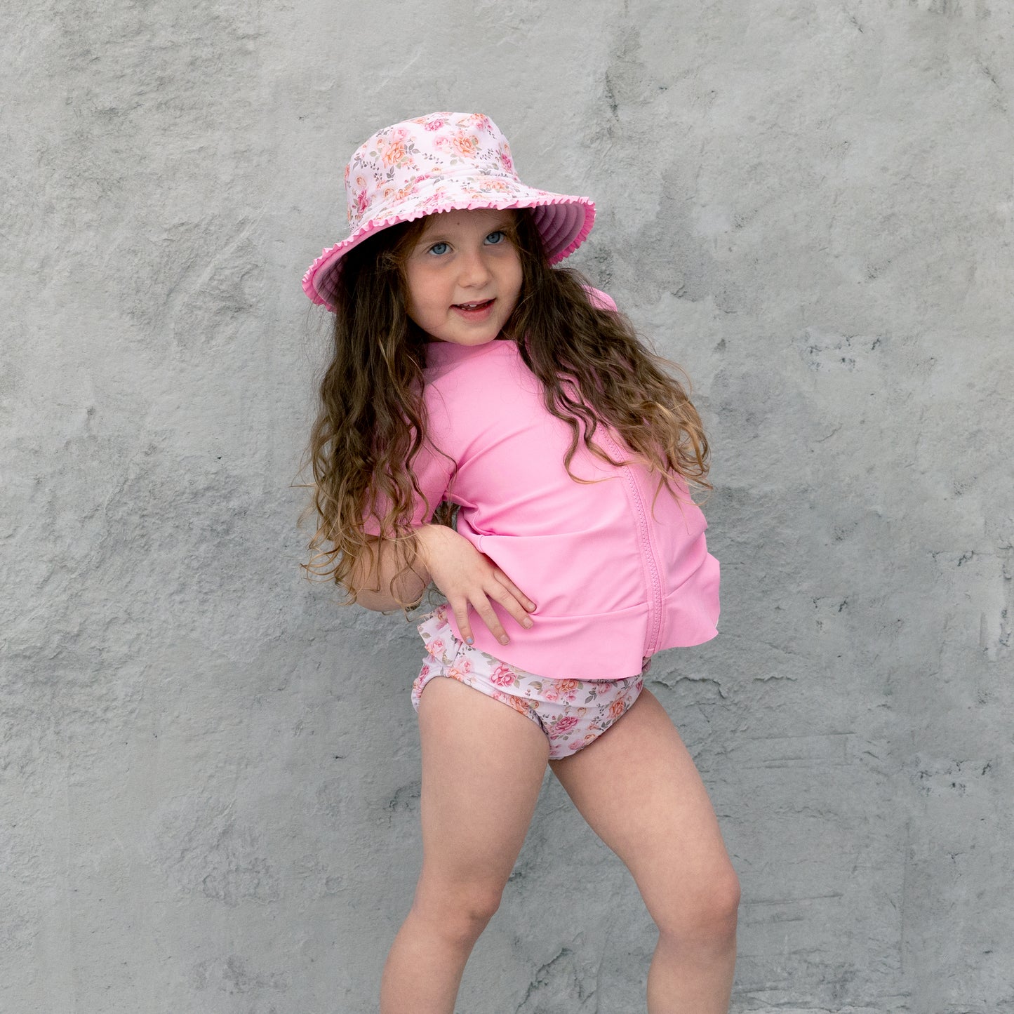 Child wearing a pink sun hat and matching outfit against a gray background