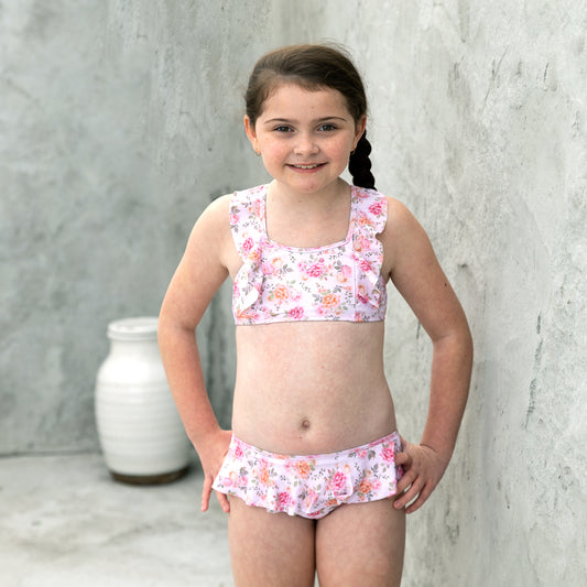 Young girl wearing a floral two-piece swimsuit against a gray concrete wall.