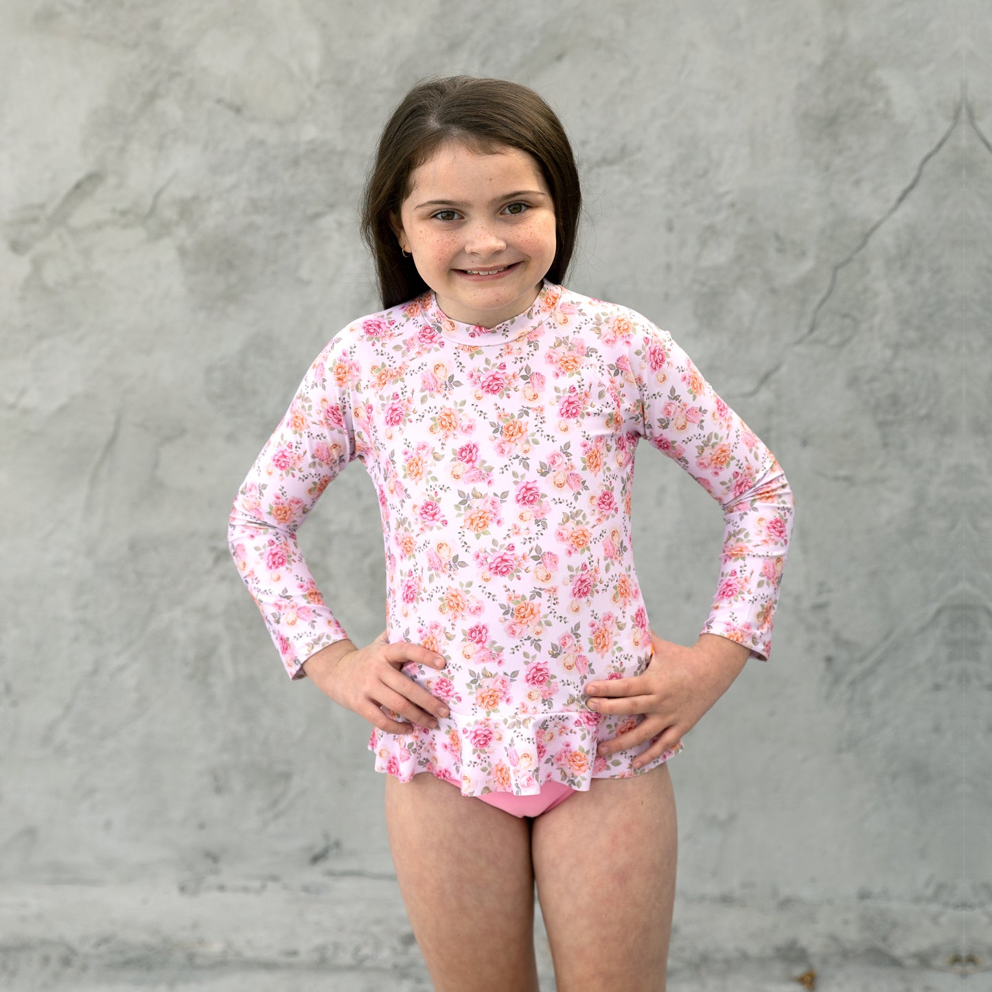 Young girl wearing a floral long-sleeve rash guard against a gray background