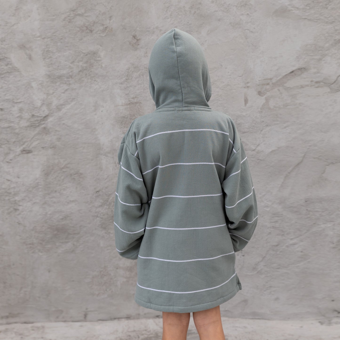 Boy wearing a gray hooded jacket with white stripes against a textured gray wall.