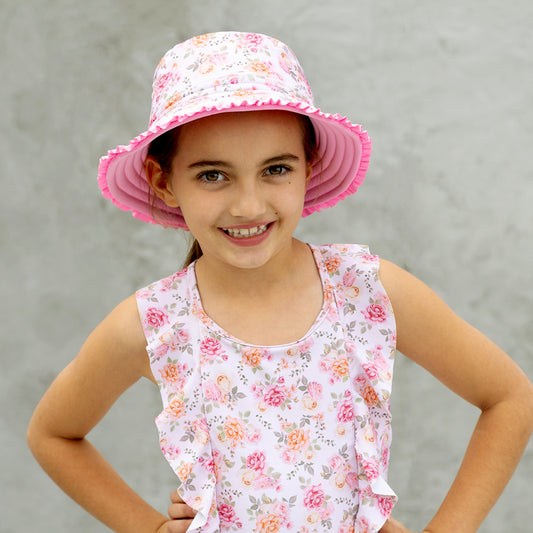 Young girl wearing a pink floral hat and matching sleeveless top against a gray background