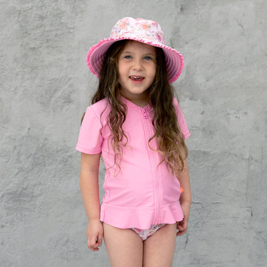 Young girl wearing a pink outfit and hat against a gray background