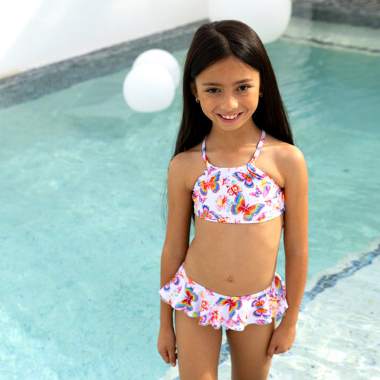 Young girl wearing a colorful butterfly-patterned bikini by a pool.