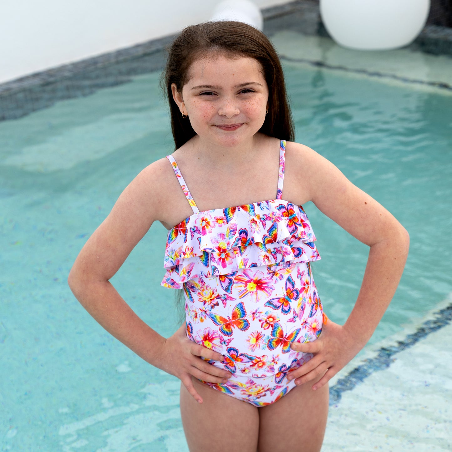 Young girl in a colorful swimsuit standing by a pool.