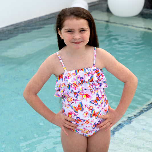 Young girl in a colorful swimsuit standing by a pool.