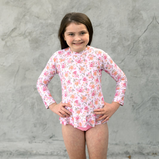 Young girl wearing a floral long-sleeve rash guard against a gray background