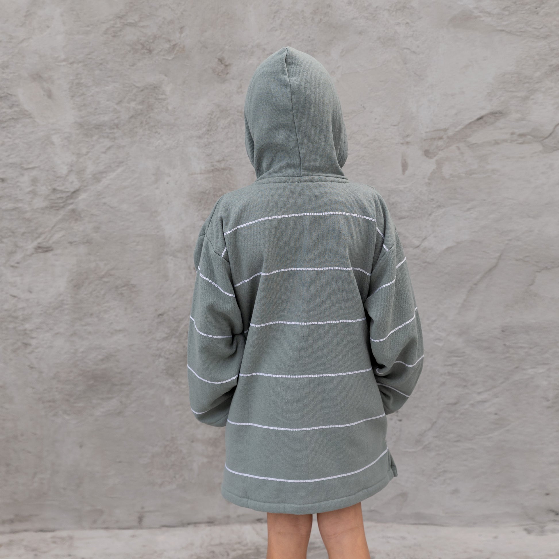 Boy wearing a gray hooded jacket with white stripes against a textured gray wall.