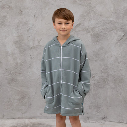 Child wearing a gray hooded towel with white stripes against a gray concrete wall.