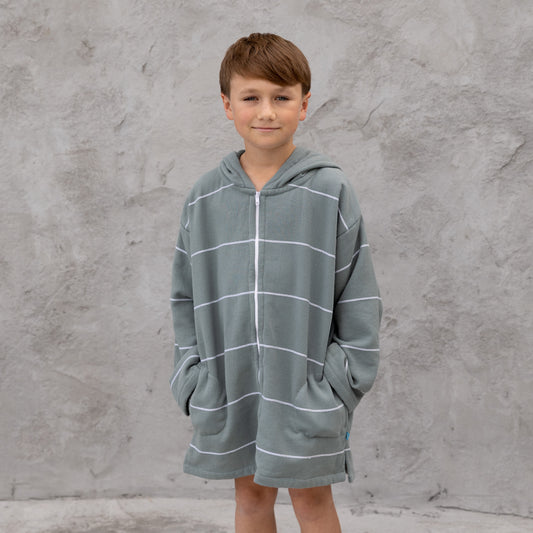 Child wearing a gray hooded towel with white stripes against a gray concrete wall.