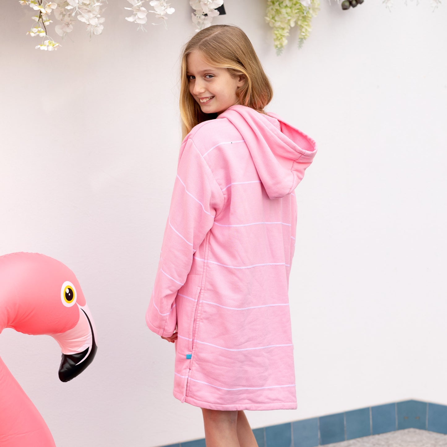 Person wearing a pink hooded towel with a flamingo floaty in the foreground.