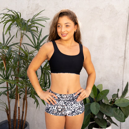 Woman wearing a black sports bra and patterned shorts standing in front of plants.