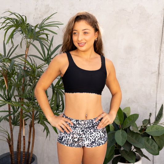 Woman wearing a black sports bra and patterned shorts standing in front of plants.