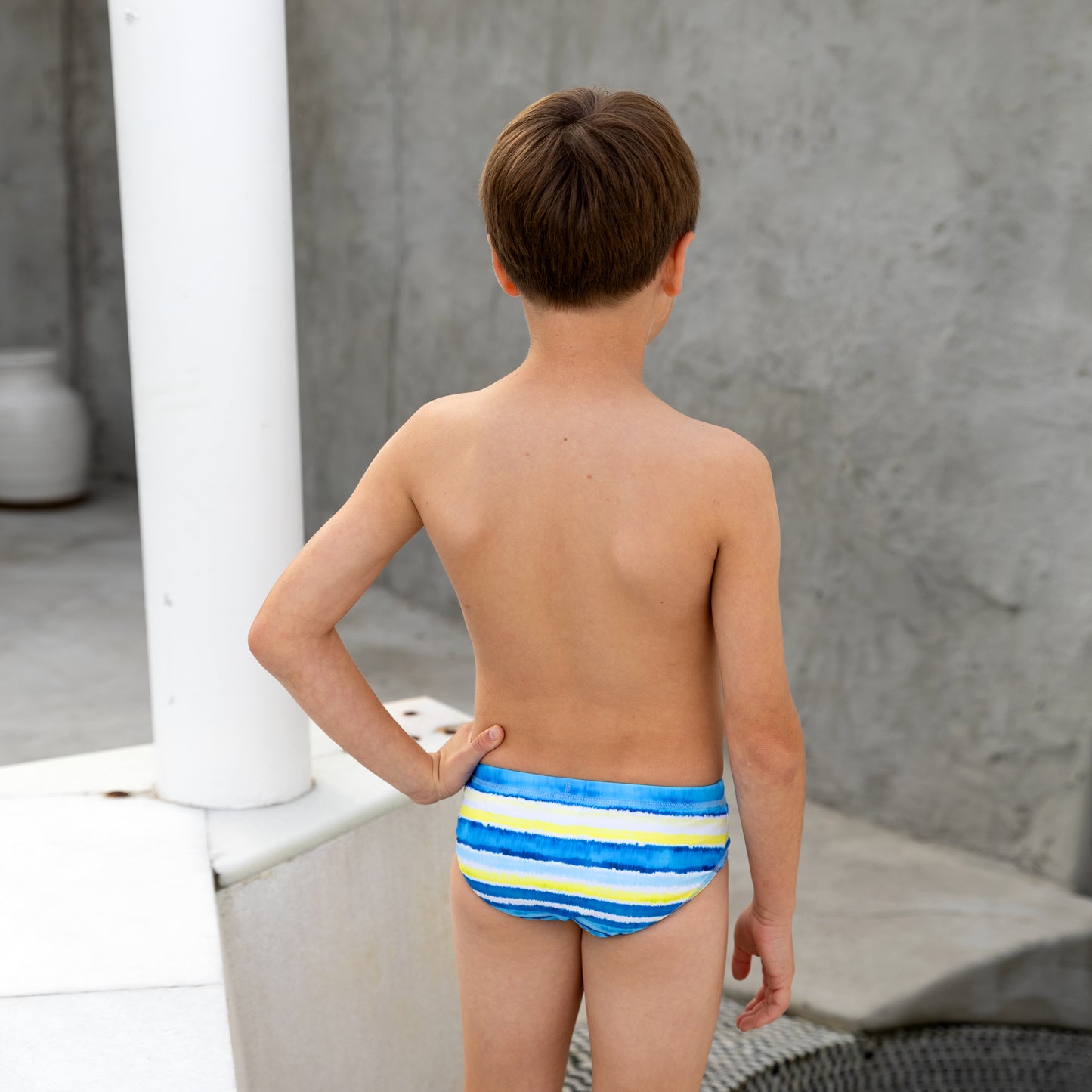 Young boy wearing a colorful striped boys swim racer against a neutral background