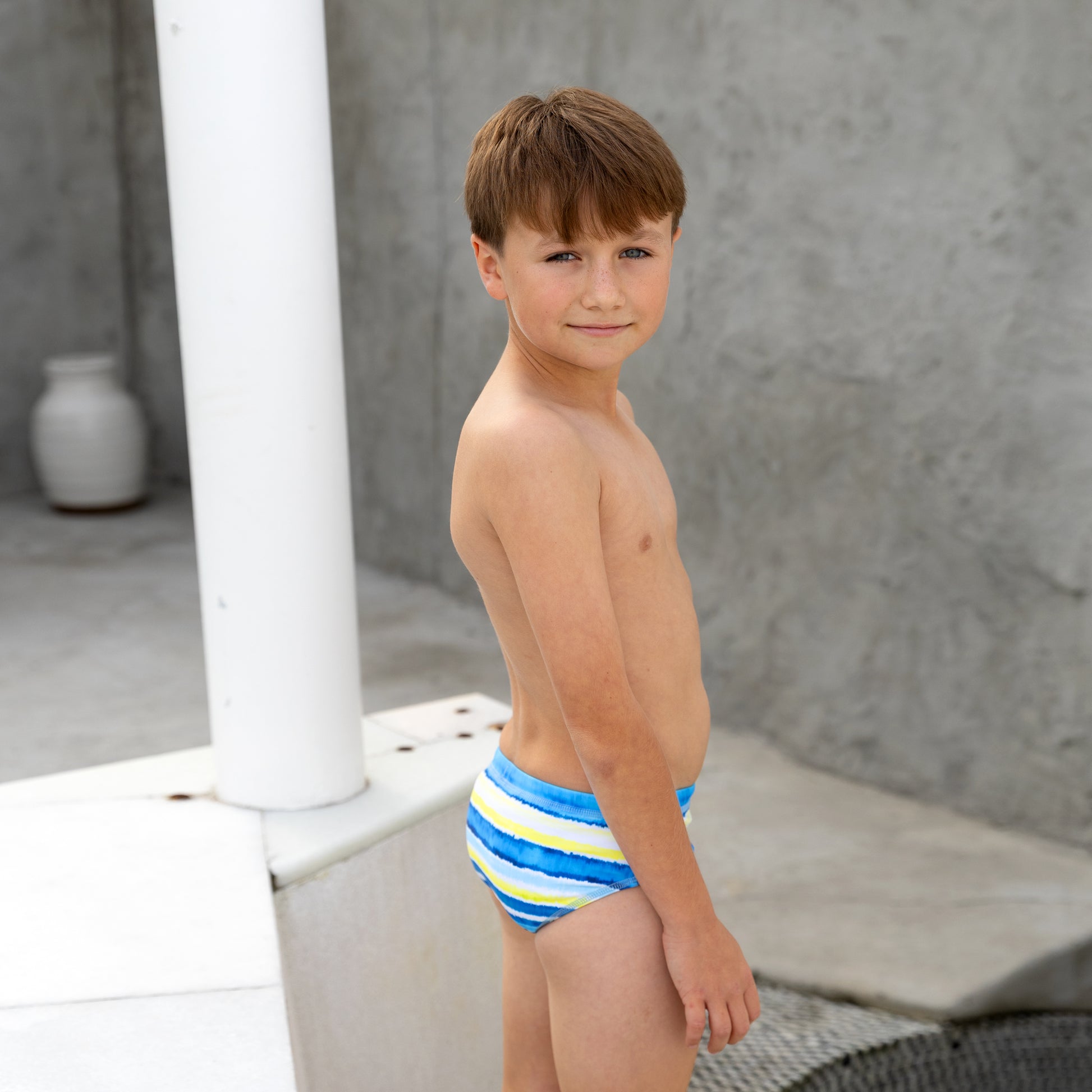 Young boy wearing a colorful striped boys swim racer against a neutral background
