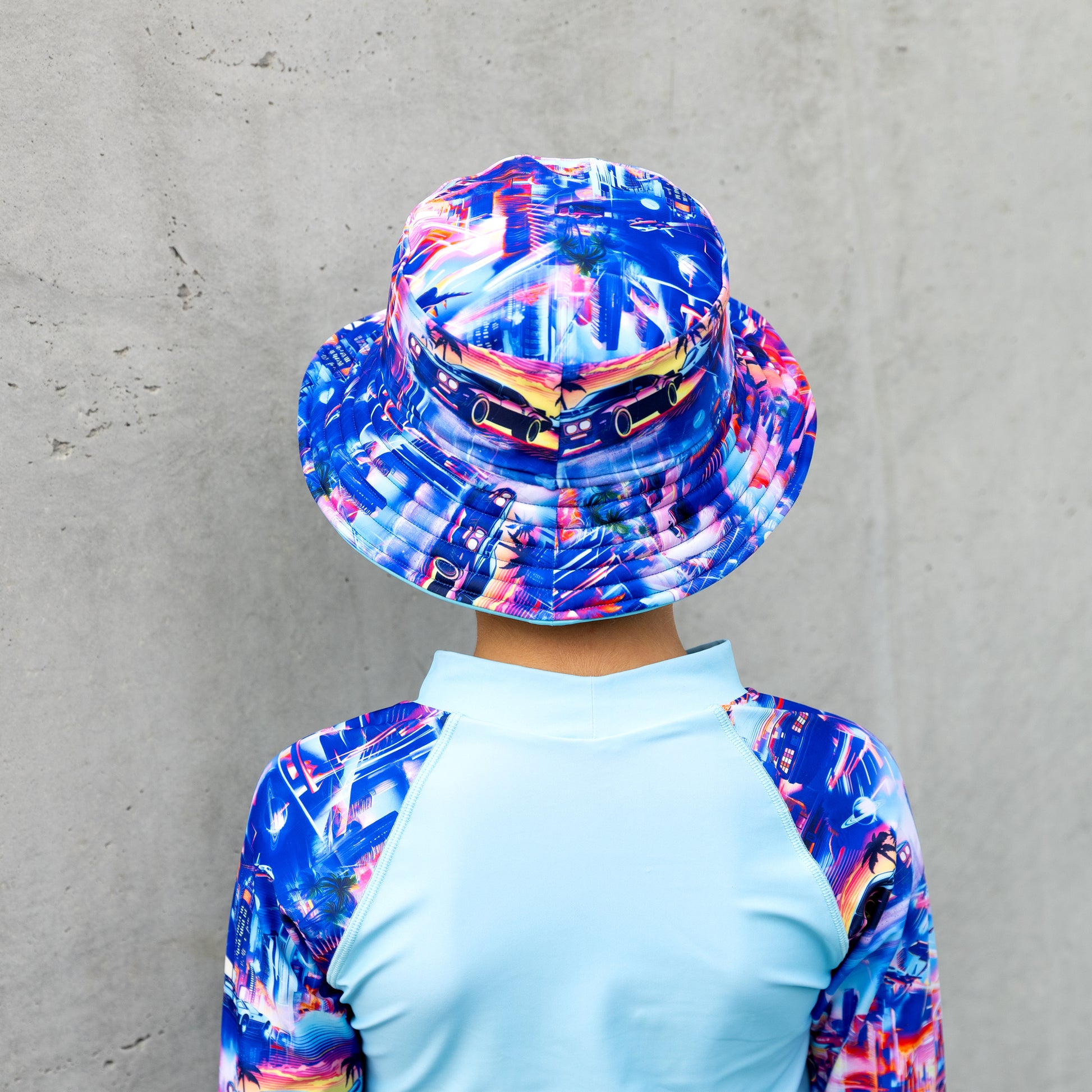 Child wearing a colorful bucket swim hat and rash guard against a gray wall