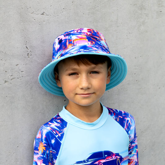 Child wearing a colorful bucket swim hat and rash guard against a gray wall