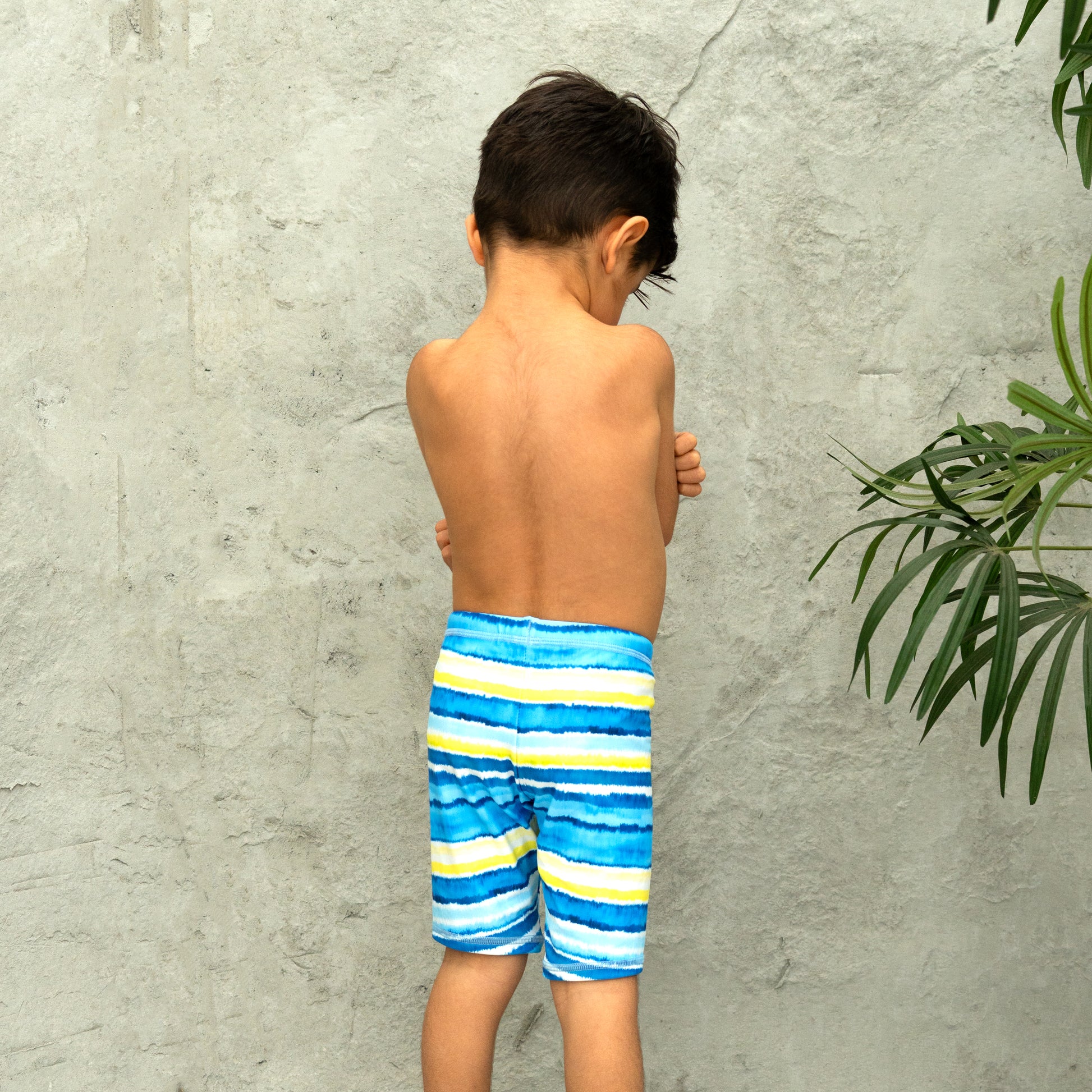 Child wearing blue striped boys swim shorts against a gray concrete wall