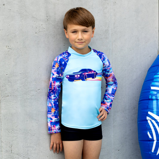 Child wearing a boy long sleeve  rashie with a blue and white inflatable ring next to them against a concrete wall.